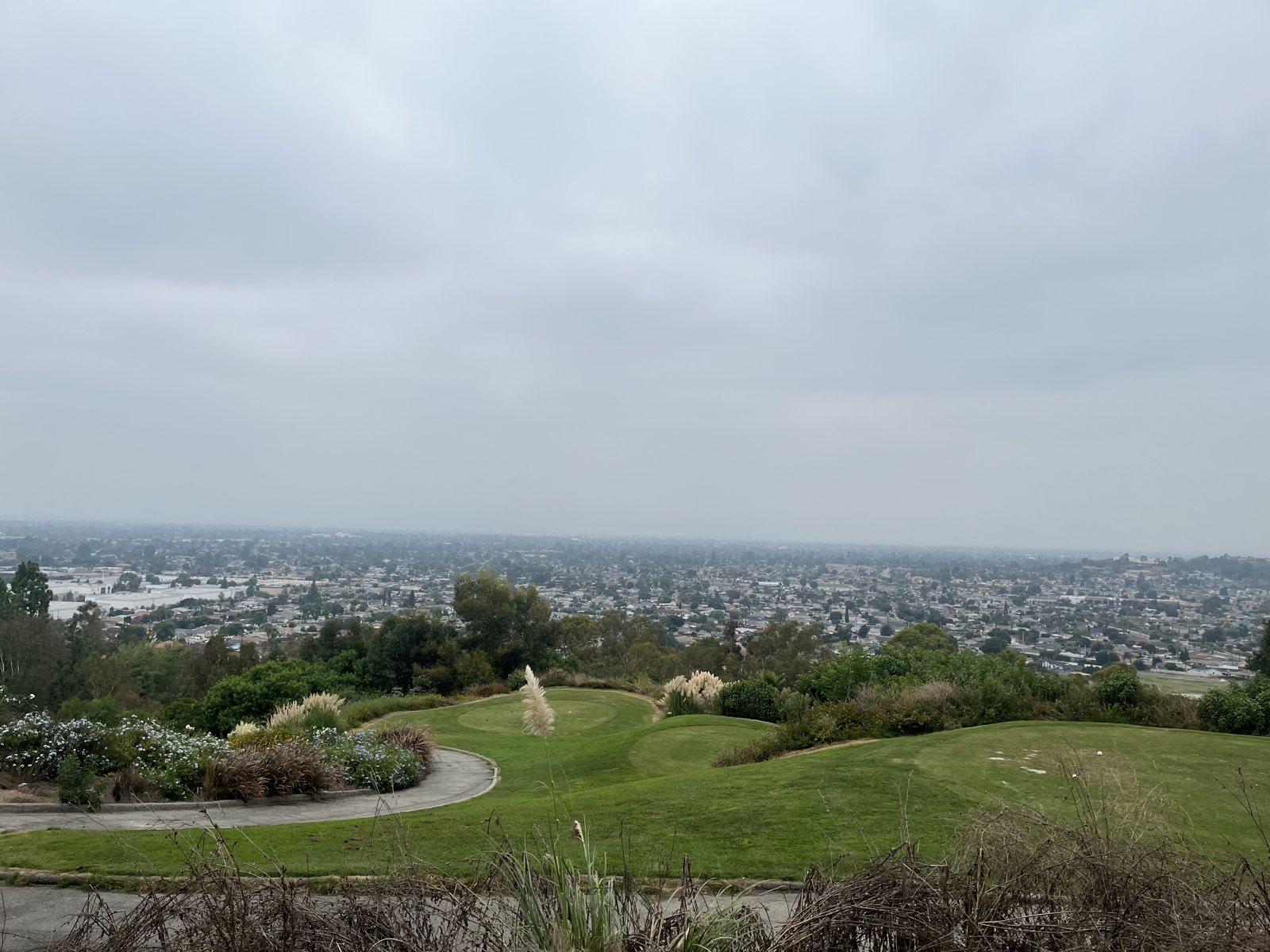 A green fairway on a hill under grey cloud, a city spread out in the haze below