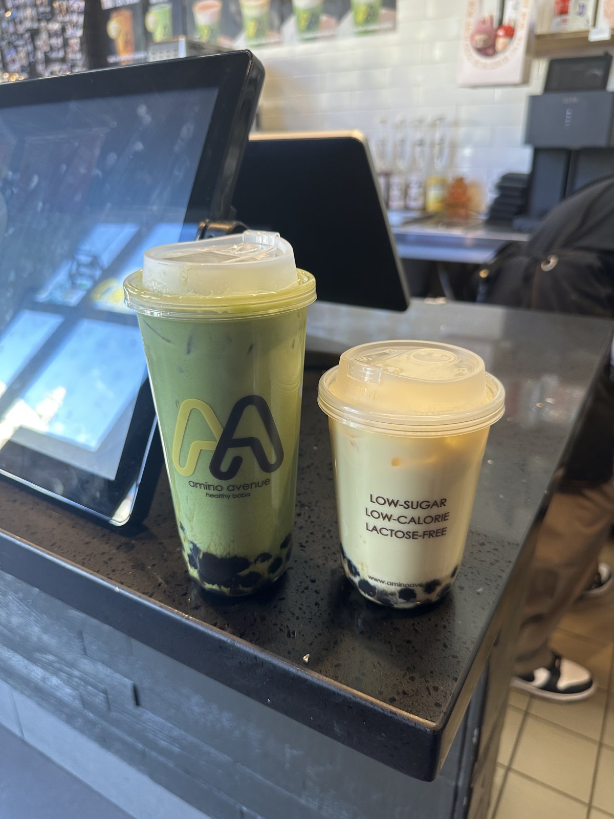 Two boba drinks on a counter, one matcha and one milk tea