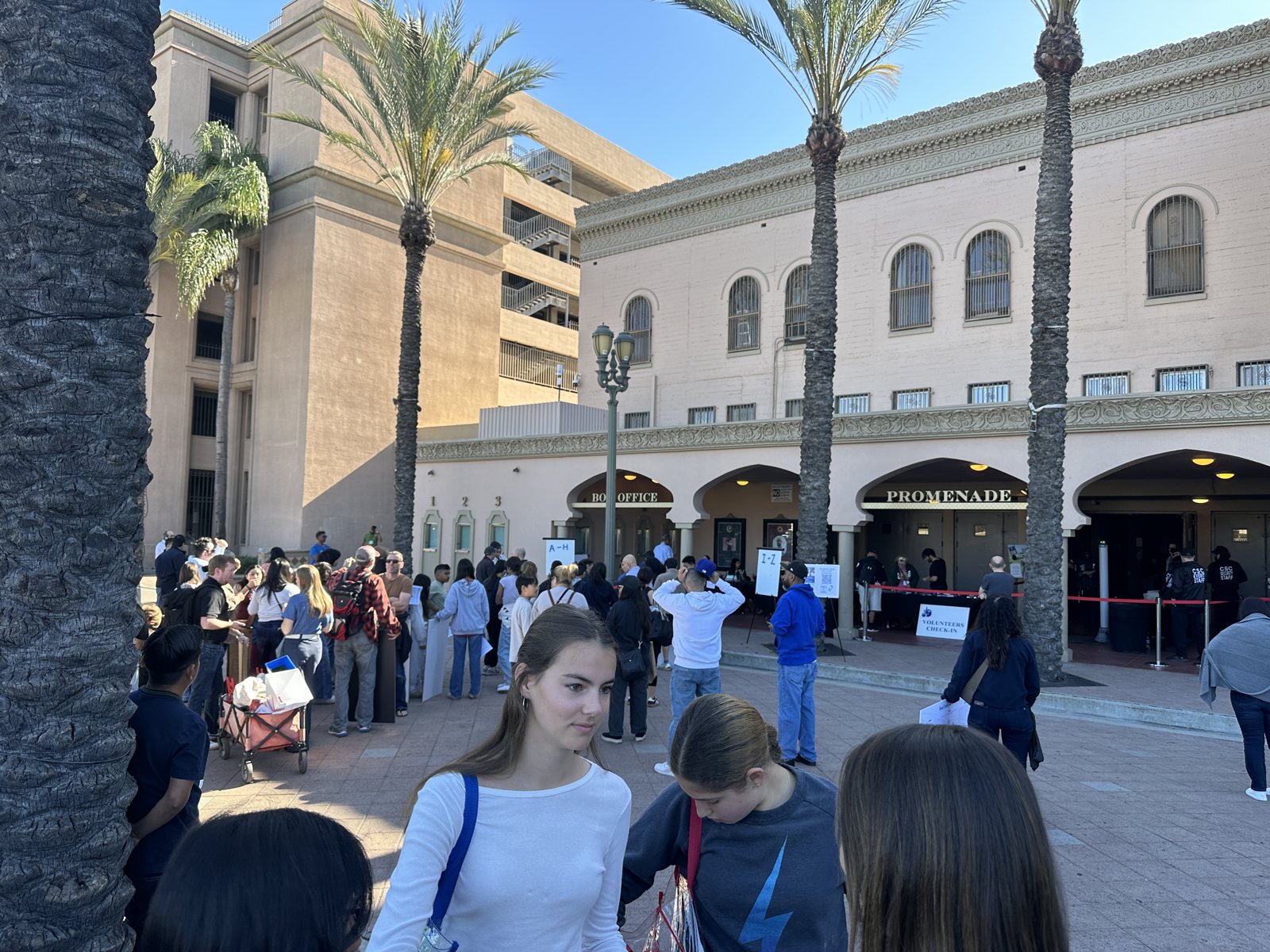 Students queueing outside a Spanish-style building with palm trees, a Promenade sign over the entrance