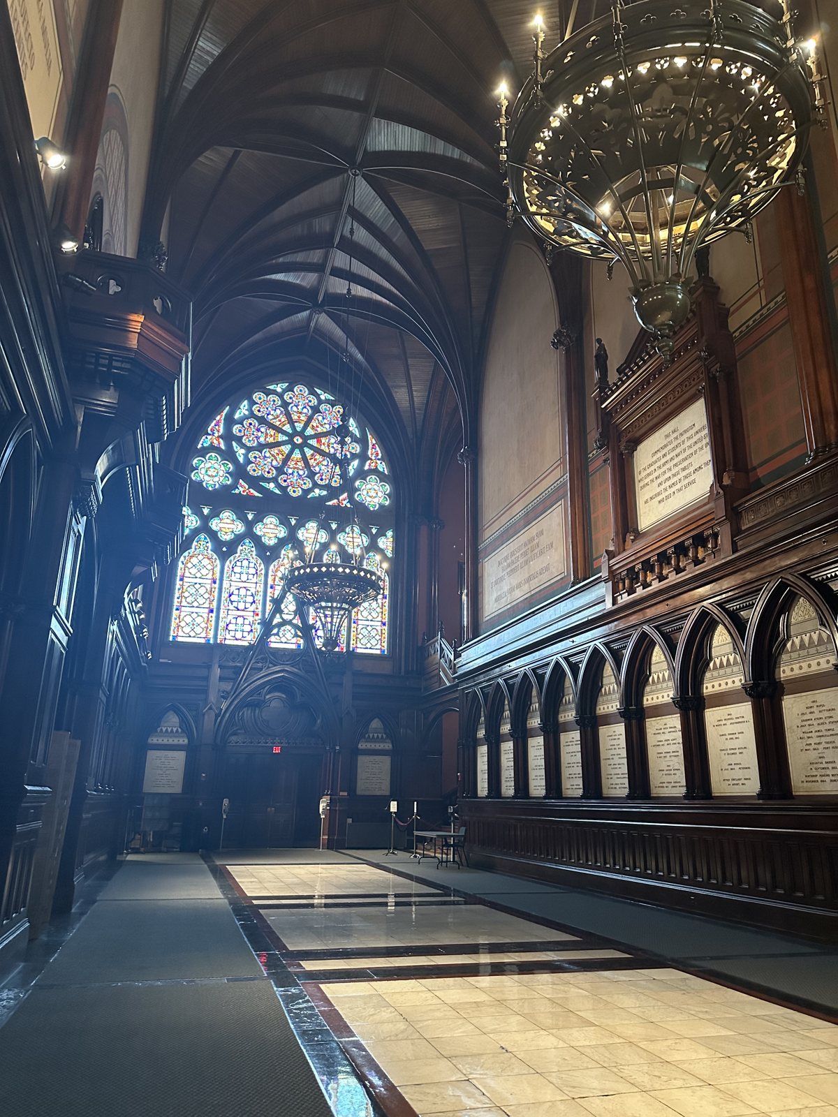 The vaulted interior of a Harvard hall, stained glass at the far end and chandeliers overhead