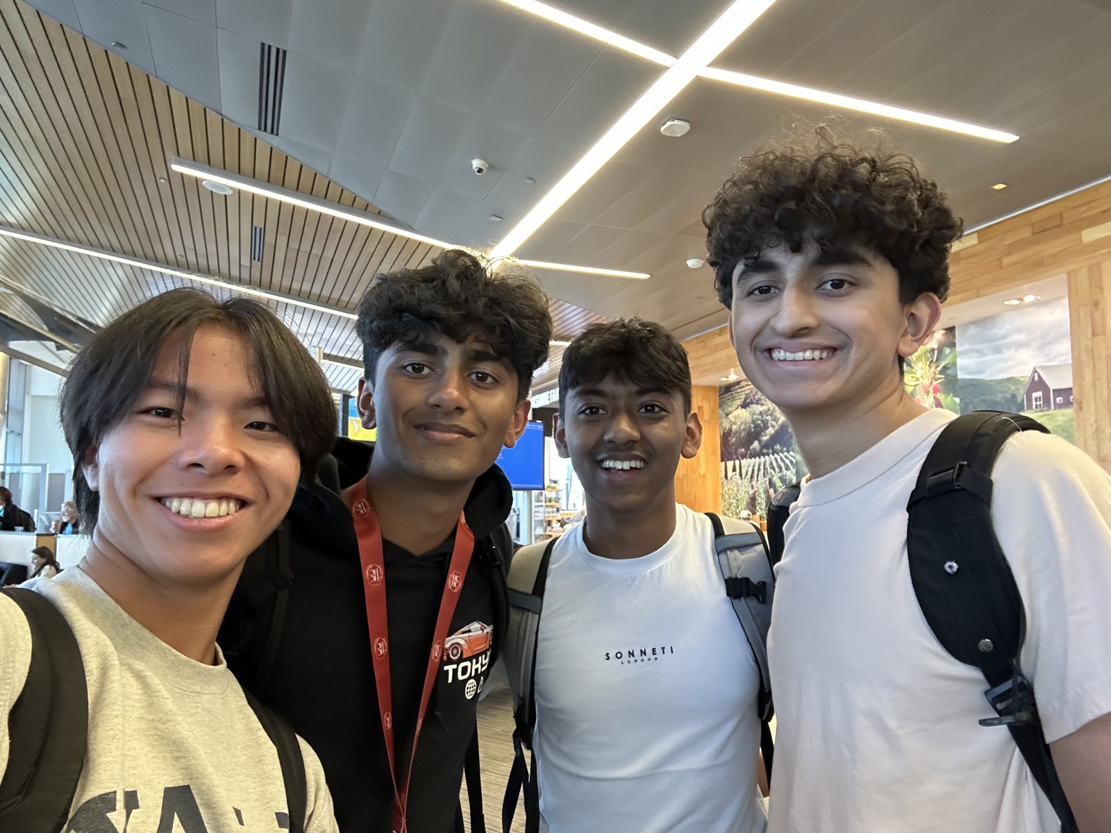 Four teammates in a selfie under a wood-slatted ceiling, all smiling