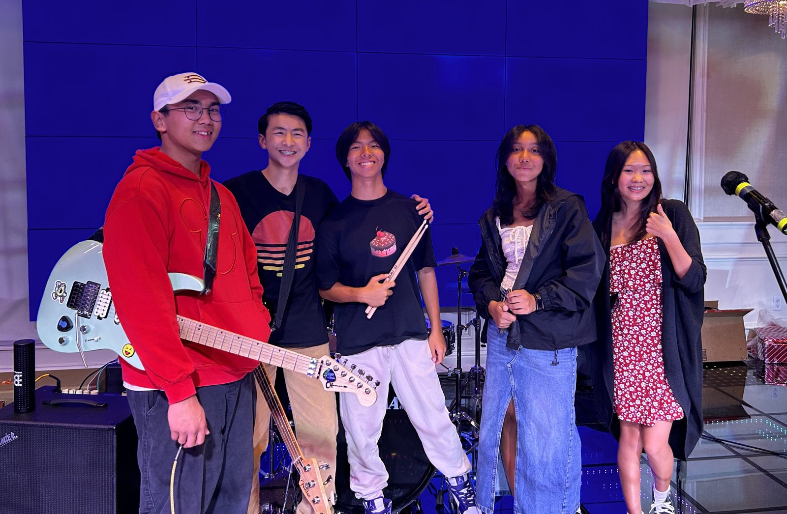 Five band members posing on a blue-lit stage with guitars and a microphone