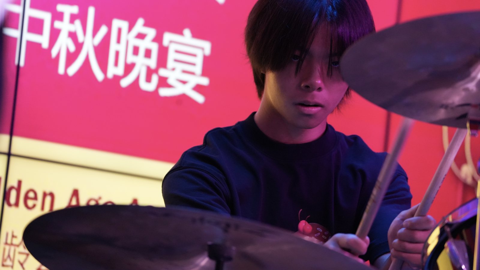 Jalen at the drum kit in a white T-shirt, a red Mid-Autumn banquet banner in Chinese characters behind him