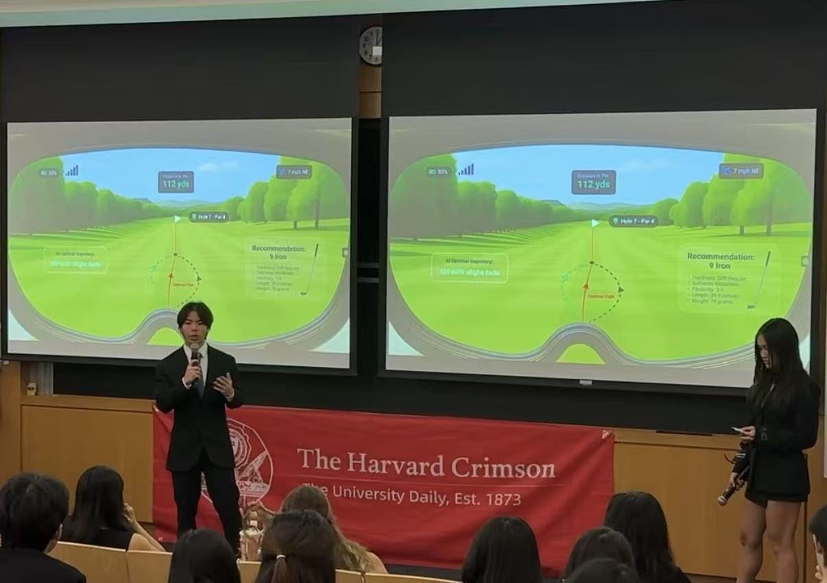 Jalen pitching with a microphone in a lecture hall, two screens behind him showing a golf heads-up display, a Harvard Crimson banner across the front