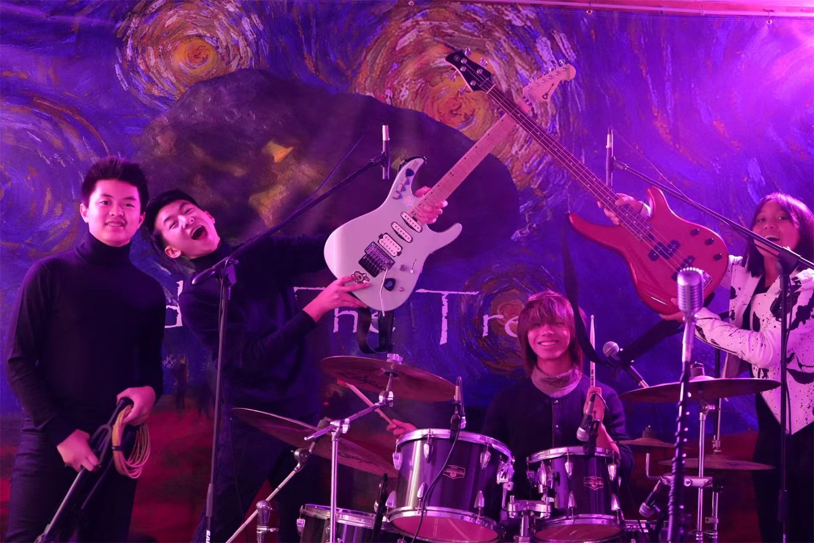 Post-Credits on stage under purple light in front of a Starry Night backdrop: two guitars held up, a bass, and the drum kit centre stage