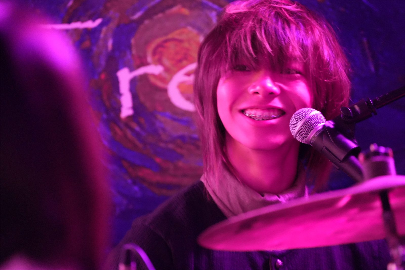 Jalen grinning at the drum kit under purple stage light, a microphone in front of him and a Starry Night backdrop behind