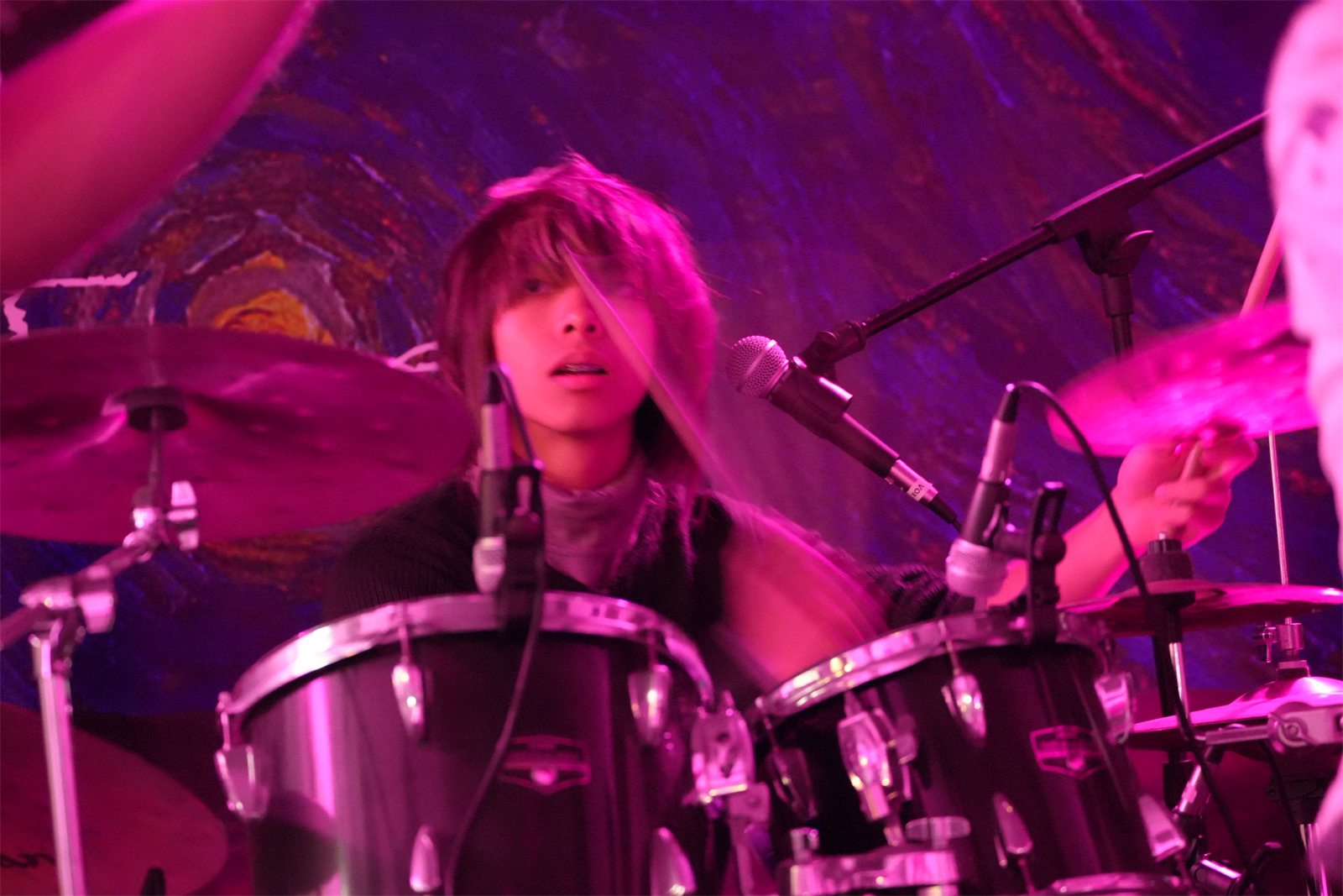Jalen at the drums, sticks blurred, looking up through his hair toward the singer
