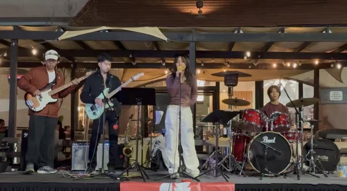 Post-Credits playing on a small outdoor stage under string lights, bass, guitar and singer up front and the drum kit at the back