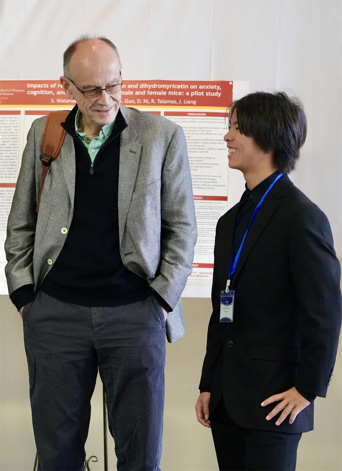 Jalen, in a black suit with a conference lanyard, laughing with Dr. Thomas Südhof in front of a poster on dihydromyricetin, anxiety and cognition in mice
