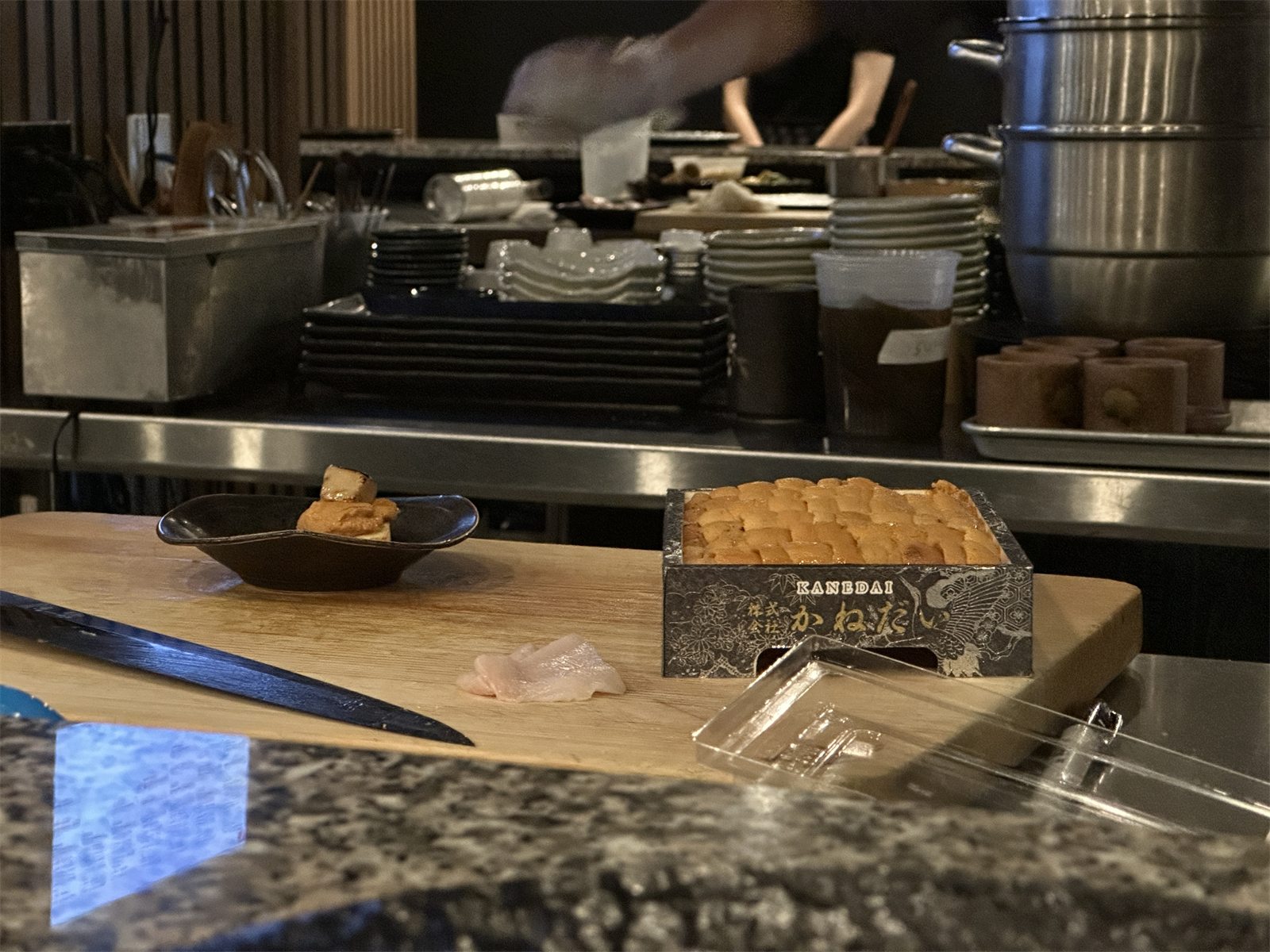 A tray of sea urchin beside a small plate of nigiri on the cutting board at a sushi counter
