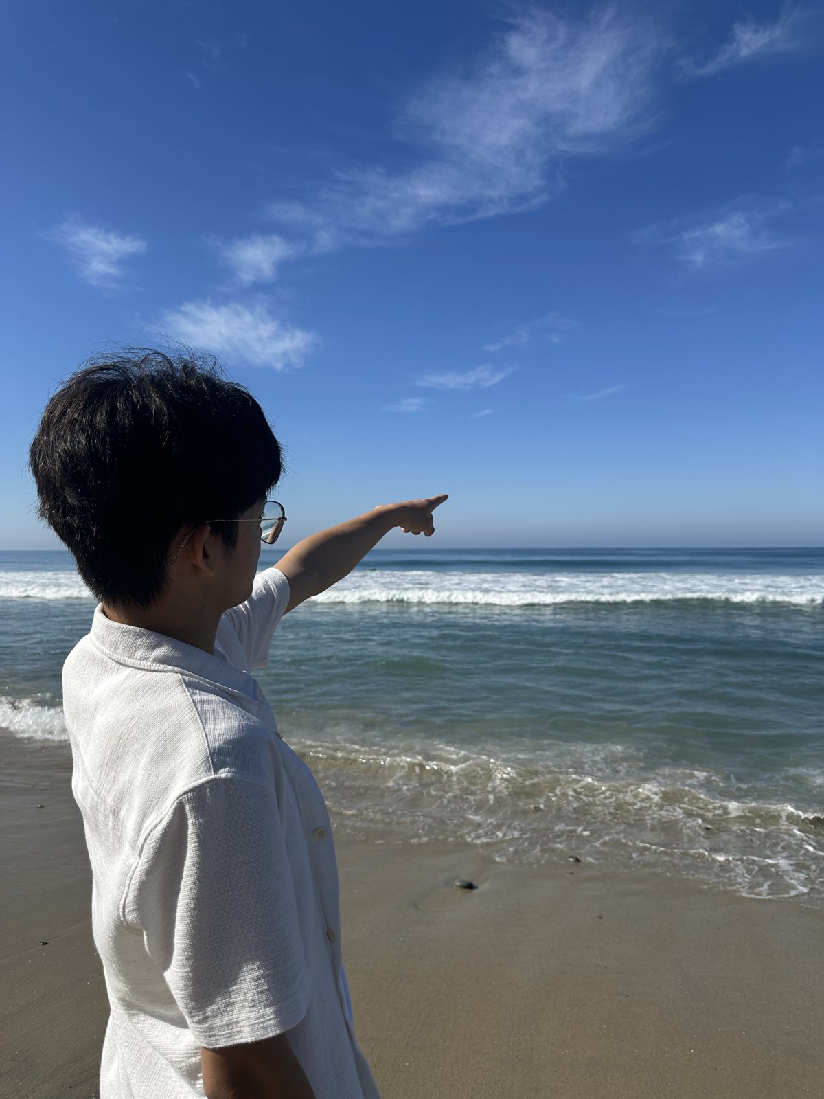 Jalen in a white T-shirt pointing out to sea from a sunny beach